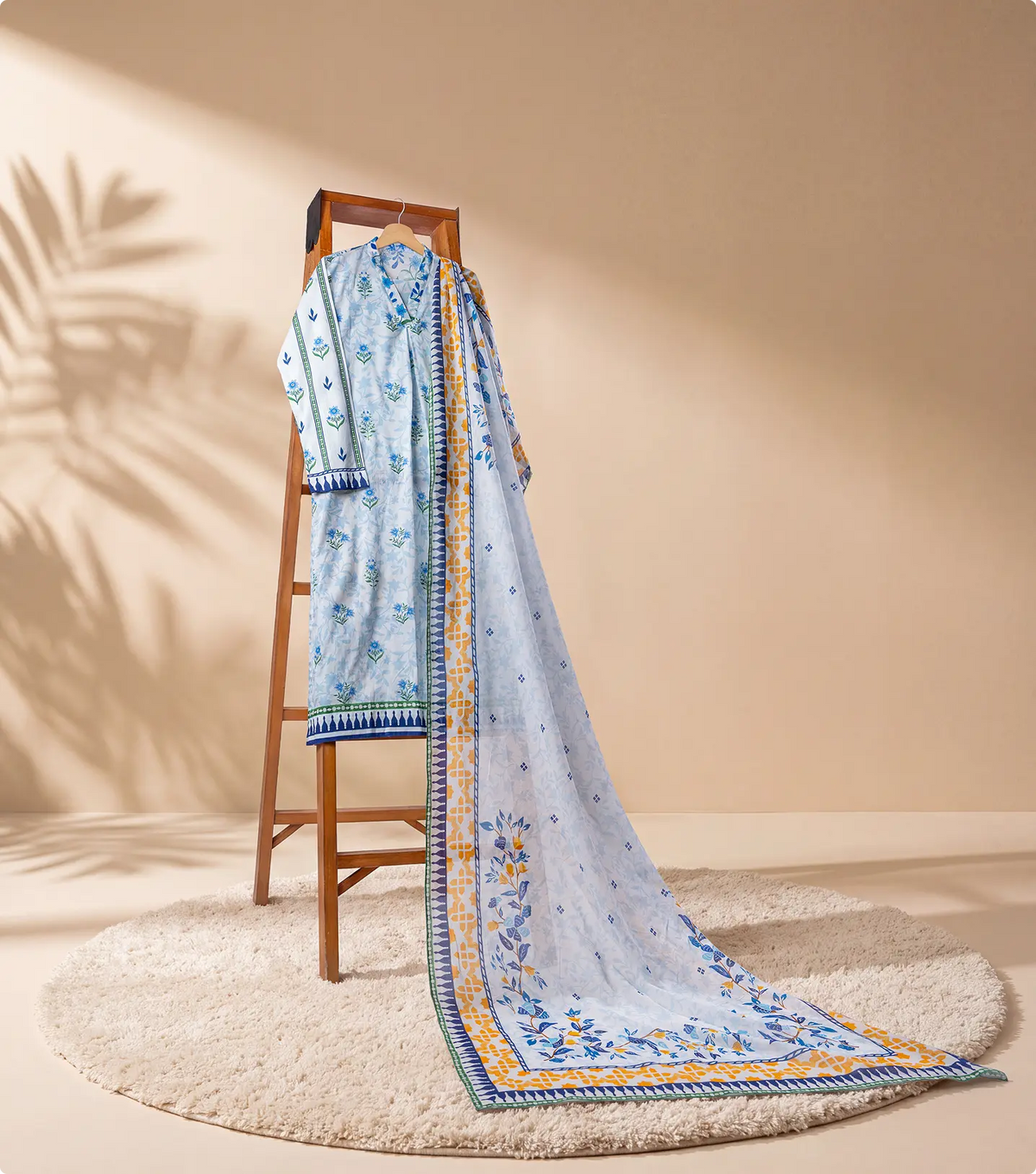 Ivory and blue 3 piece unstitched lawn suit on a wooden ladder with trailing printed dupatta
