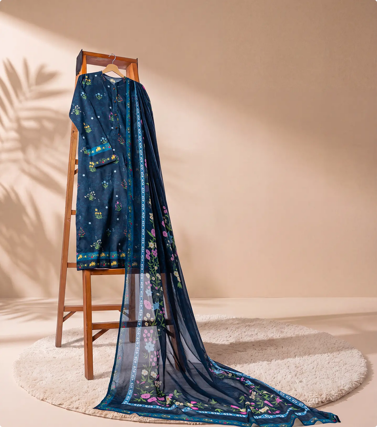Navy blue 3 piece unstitched lawn suit on a wooden ladder with trailing sheer chiffon dupatta