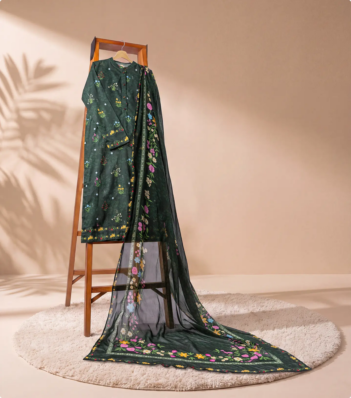 Forest green 3 piece unstitched lawn suit on a wooden ladder with trailing sheer chiffon dupatta