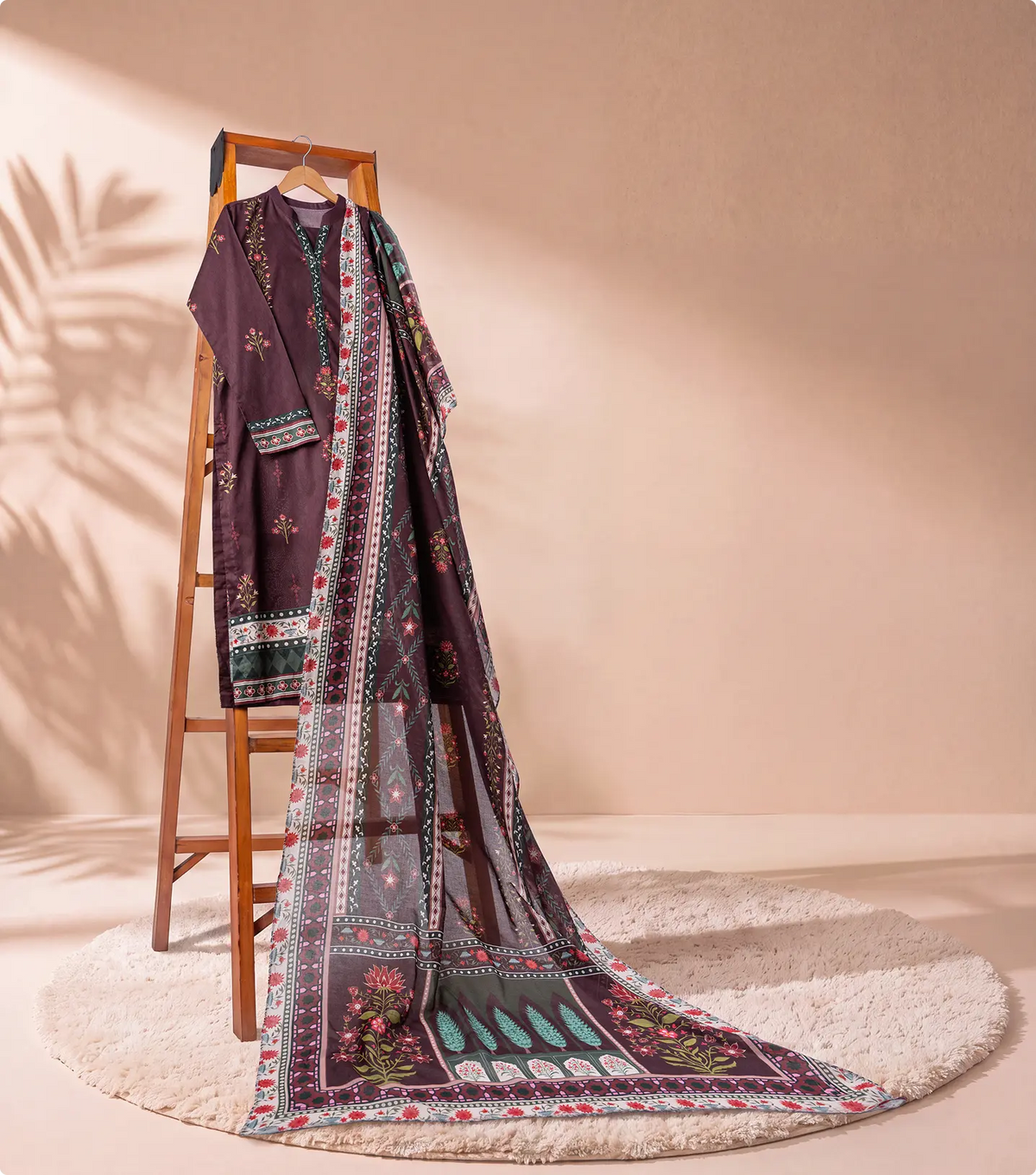Burgundy 3 piece unstitched lawn suit on a wooden ladder with trailing printed voile dupatta